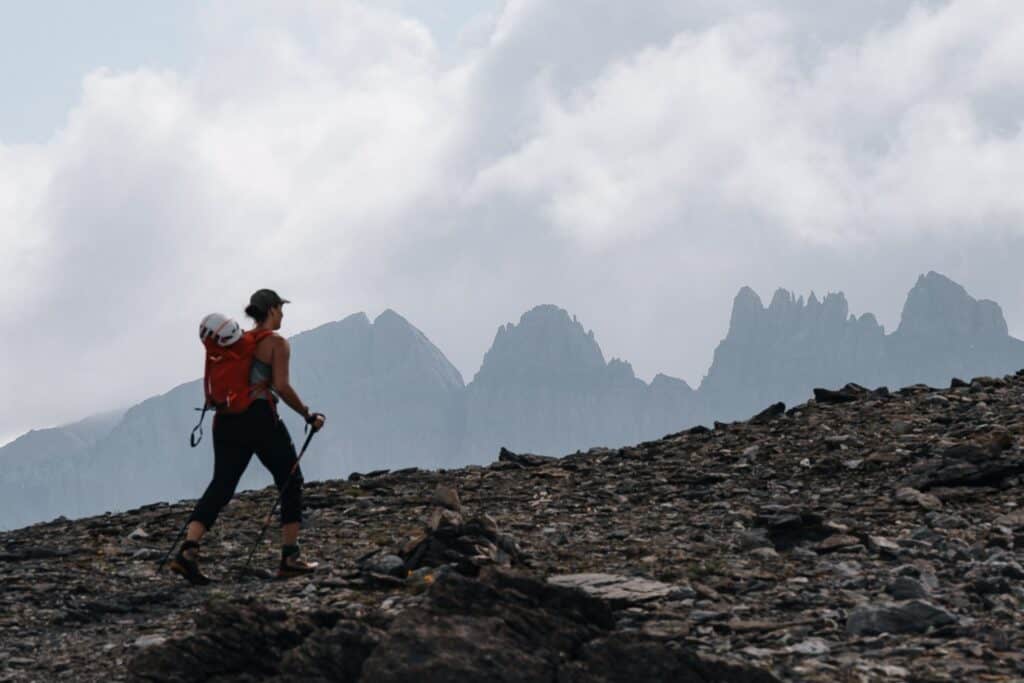 Eine Bergsteigerin auf dem Aufstieg, mit zerklüfteten Felsen und steilen Bergwänden im Hintergrund, die die Herausforderungen des Alpinismus symbolisieren.